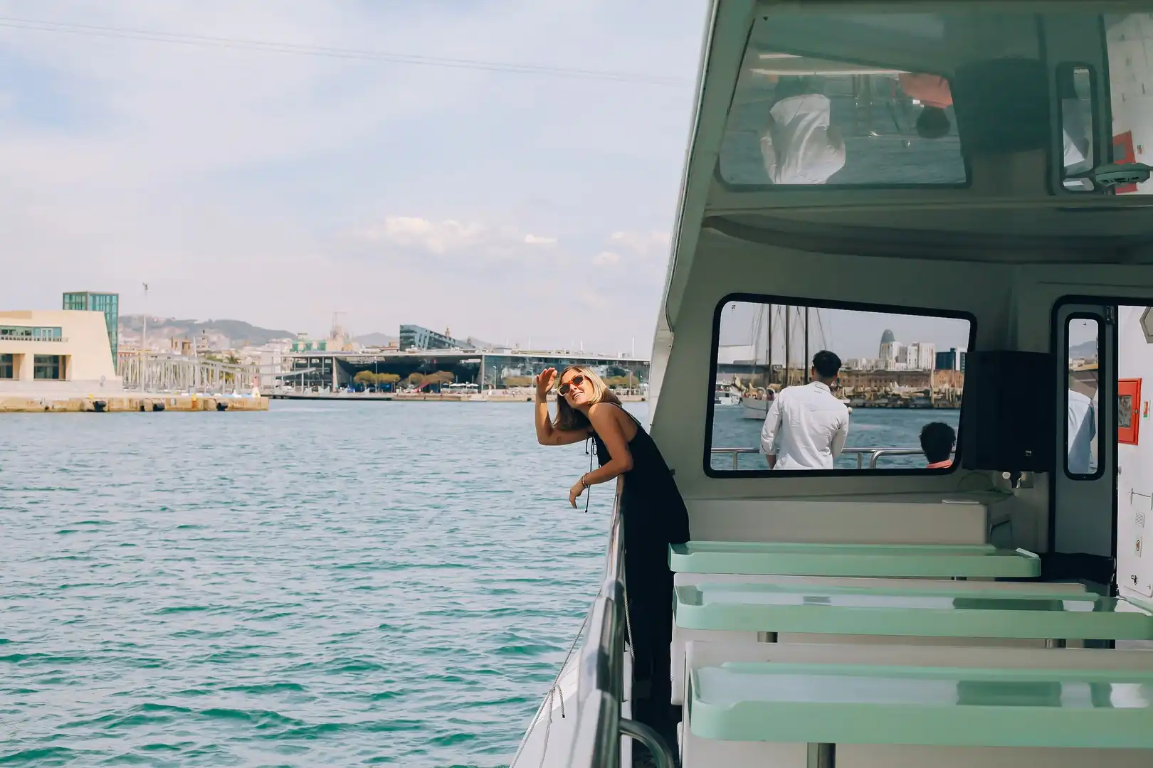 Pasajera saludando desde la barandilla del catamarán con el puerto de Barcelona al fondo