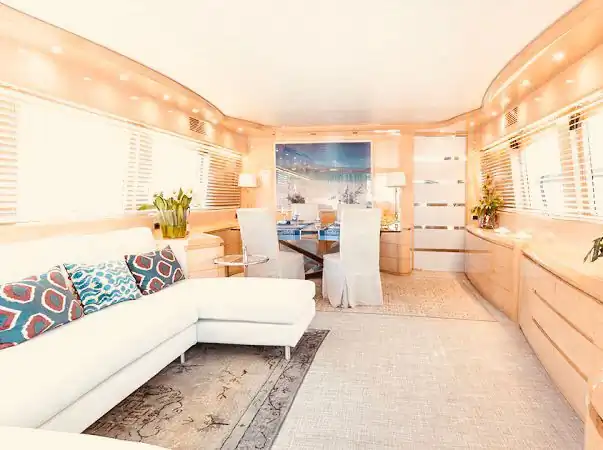 Salón interior de yate con sofá blanco en L, comedor y decoración en tonos cálidos