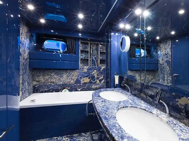 Baño de yate revestido en mármol azul con bañera y lavabo doble bajo focos